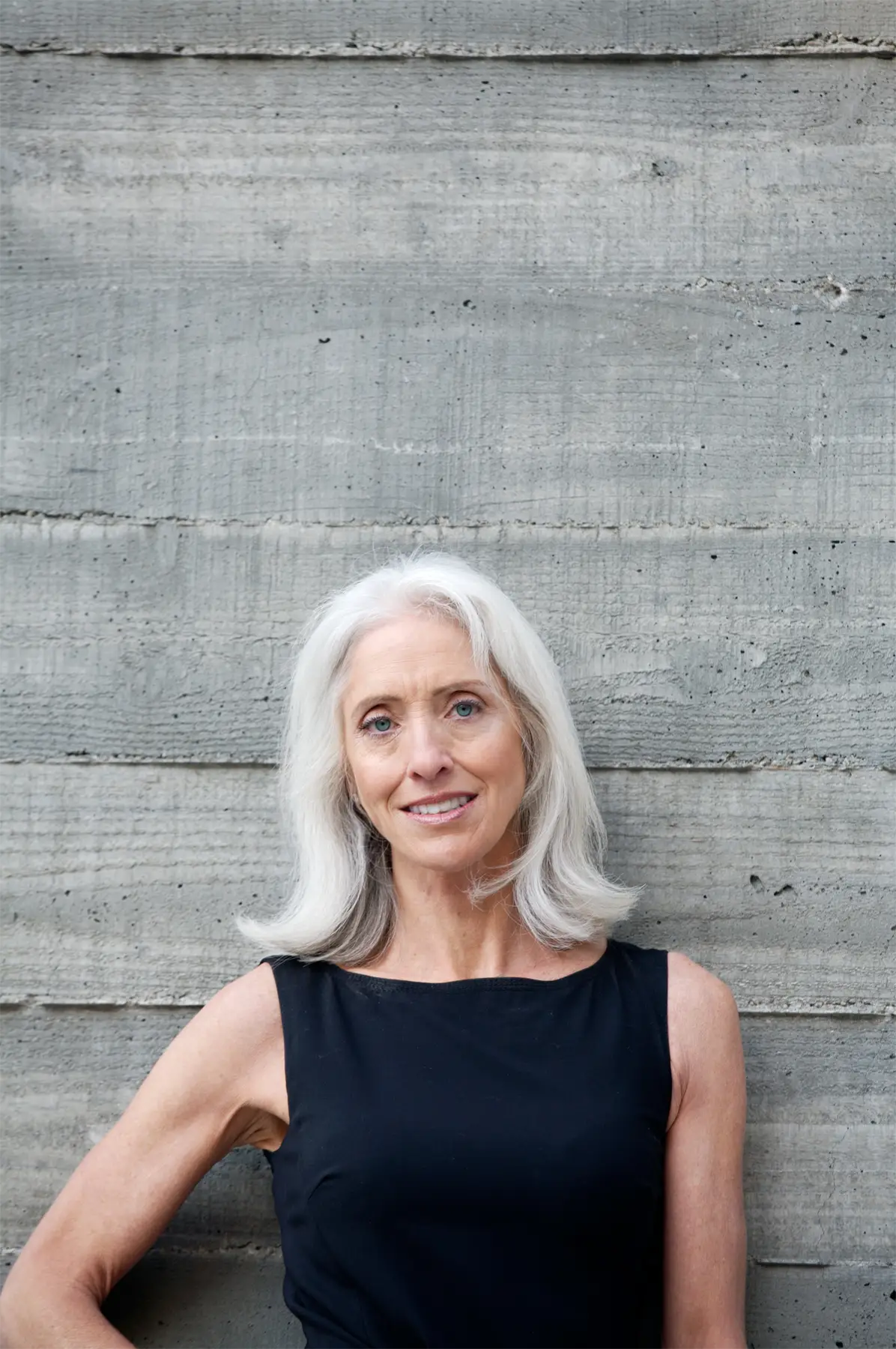 Woman with white hair in a black dress against a concrete wall